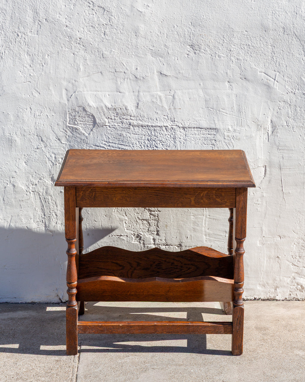 Front view of an oak side table with molded top, ring-turned legs and scalloped shelf below