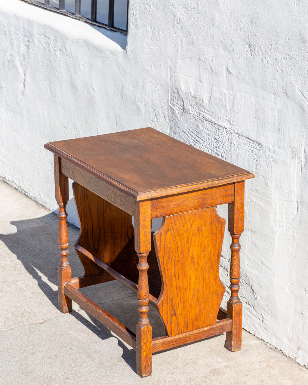 Three-quarter view from the end of an oak side table showing the shaped end panel and box stretcher
