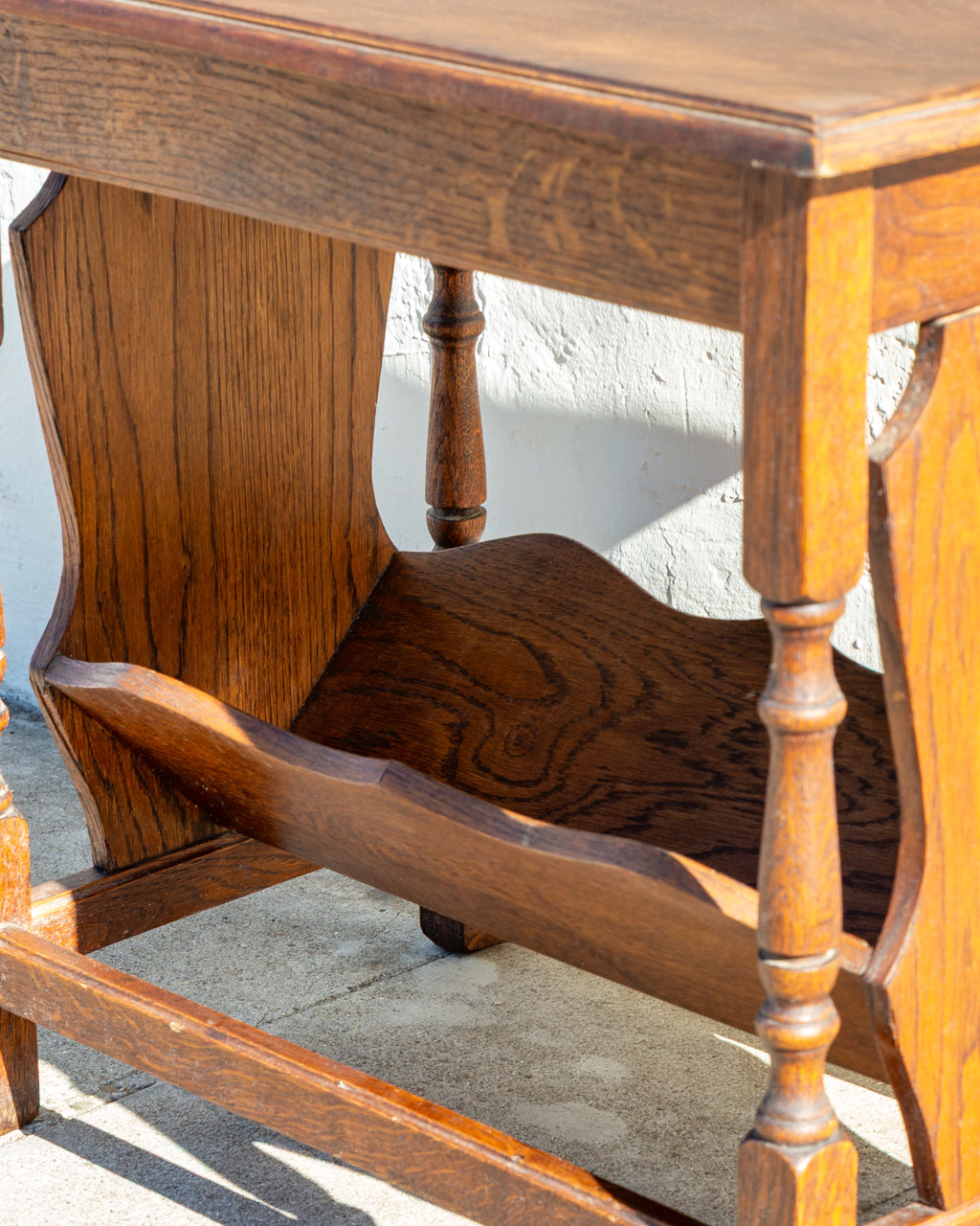 Close-up of the oak trough shelf with scalloped sides and open grain between turned legs