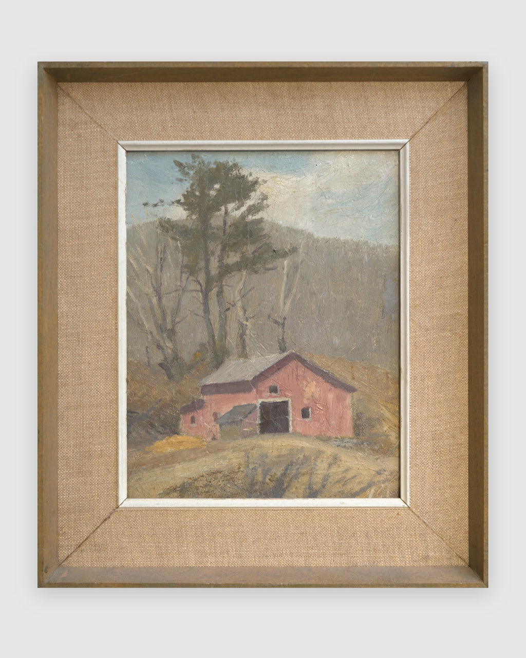 Straight-on view of a DeWitt Parshall painting of a red barn below bare trees in early spring in a wood frame with linen liner, on a light gray background.