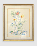 Straight-on view of a framed Picasso color lithograph of a sprouting flower bouquet in green, blue, red and yellow, cream mat with gold fillet, gilt and silver frame, on a light gray background.