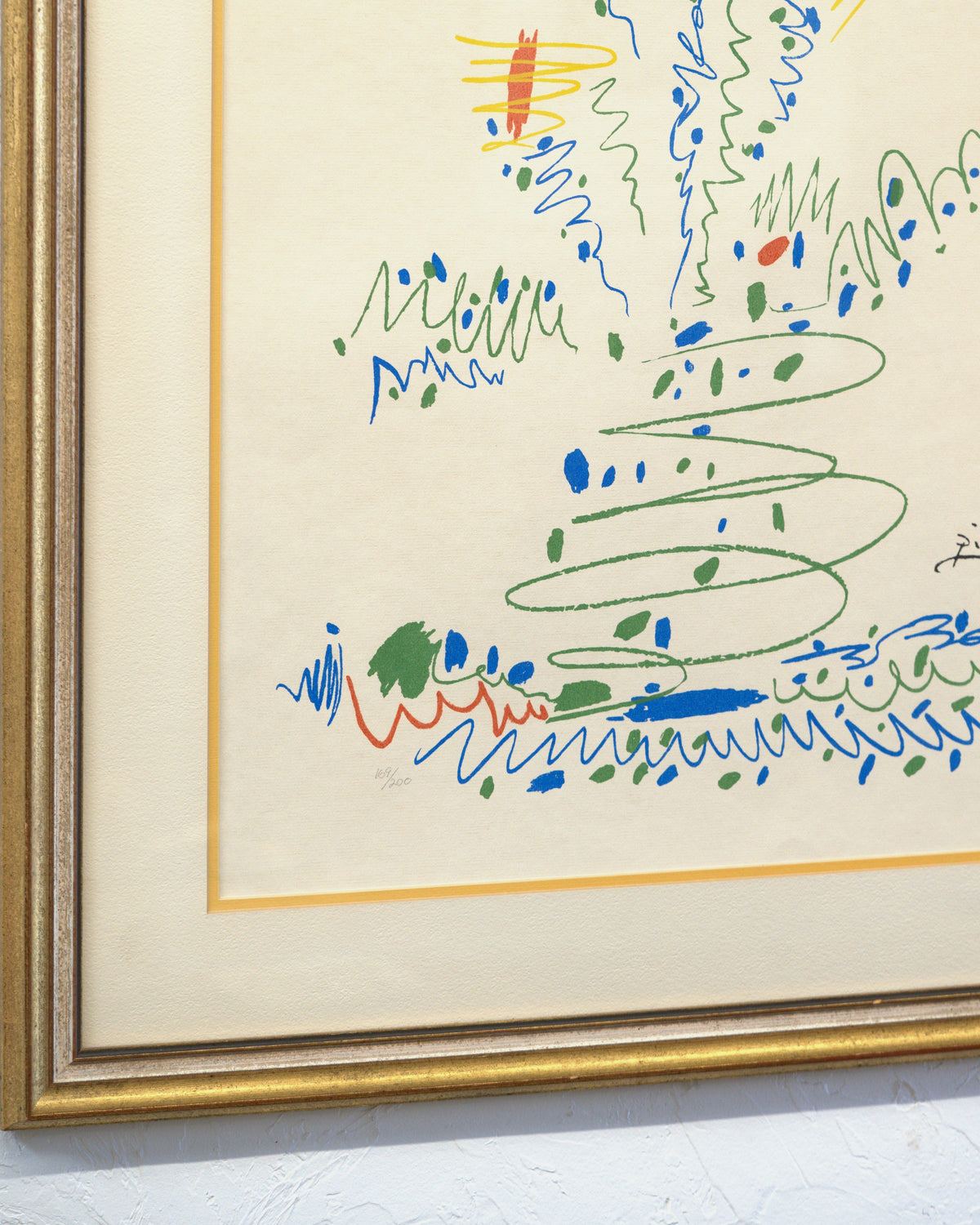 Angled view of the lower left corner of the gilt and silver wood frame, showing frame depth, mat and glazing over the Picasso lithograph.