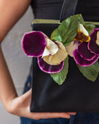 Detail of the velvet pansy appliqués and green fabric leaves against the black canvas body of the tote.