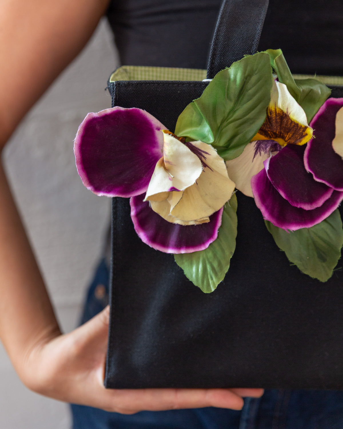 Detail of the velvet pansy appliqués and green fabric leaves against the black canvas body of the tote.