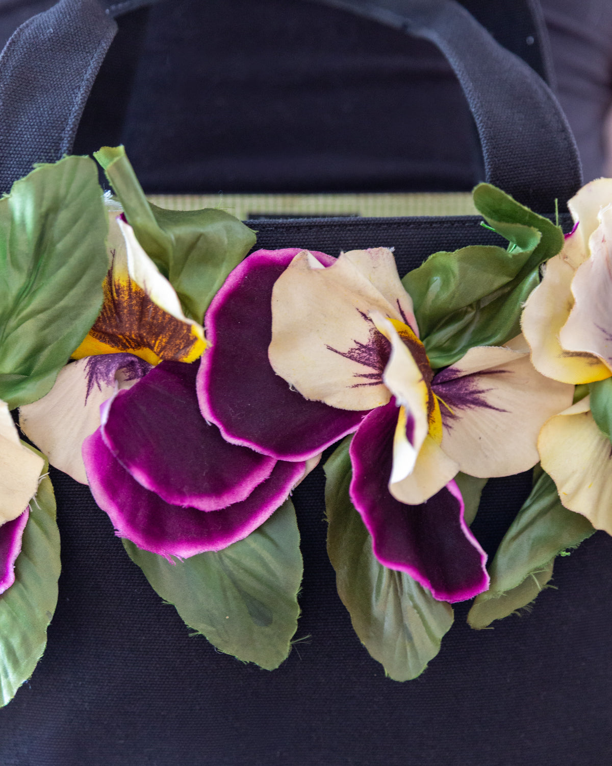 Close view of the pansy band across the tote, purple velvet petals and cream faces with purple whiskers and yellow throats.