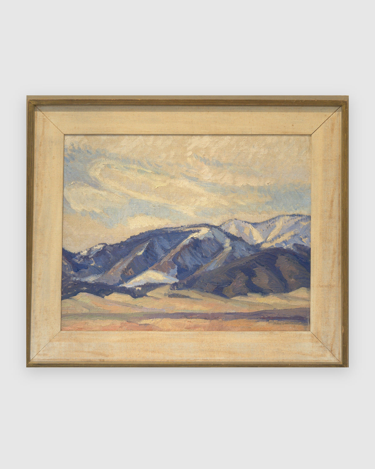 Straight-on view of a Lee Fritz Randolph painting of a blue snow-streaked mountain range above an ochre plain in a natural wood frame, on a light gray background.