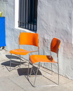 Second angled view of two orange 40/4 stacking chairs against a white stucco wall