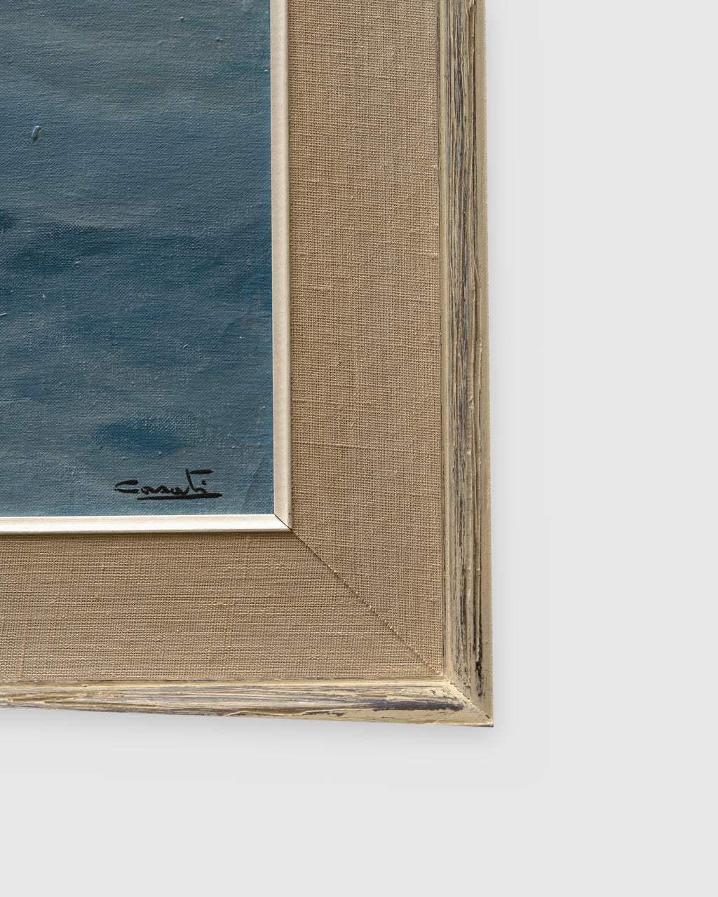 Corner of the frame on the 1960s seascape of turquoise breaking waves, rocks and a misty headland in a whitewashed frame with linen liner.