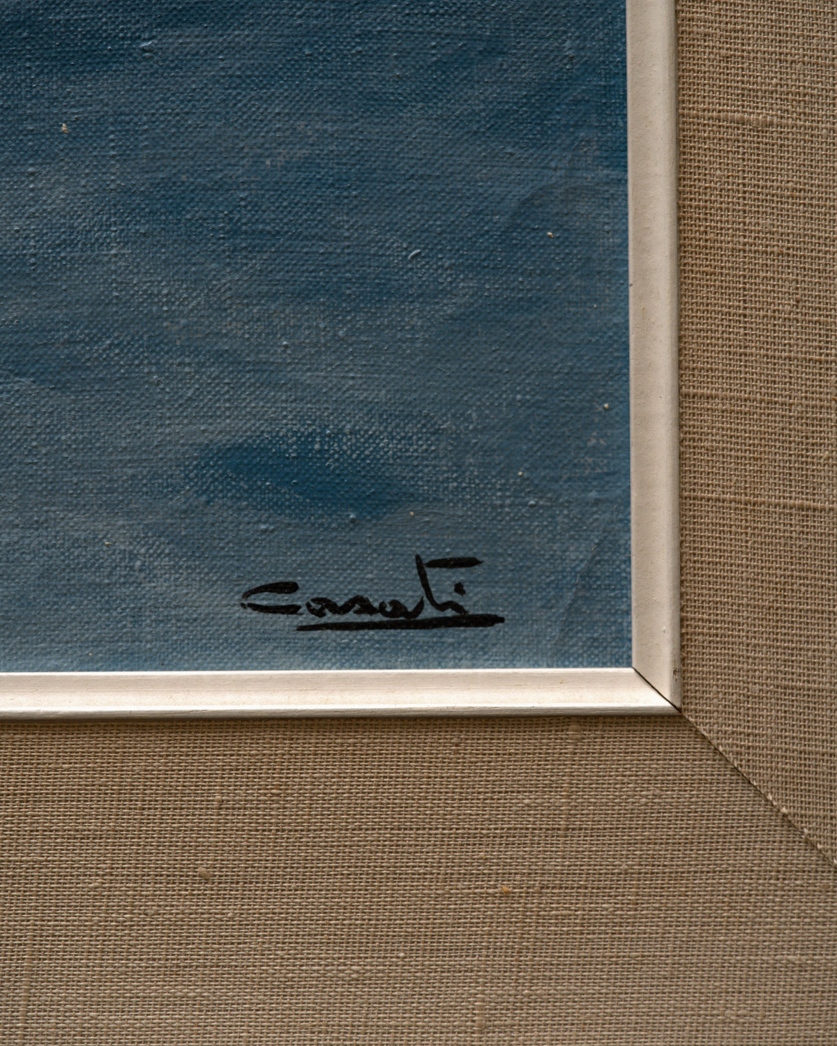 Detail of the signature on the 1960s seascape of turquoise breaking waves, rocks and a misty headland in a whitewashed frame with linen liner.