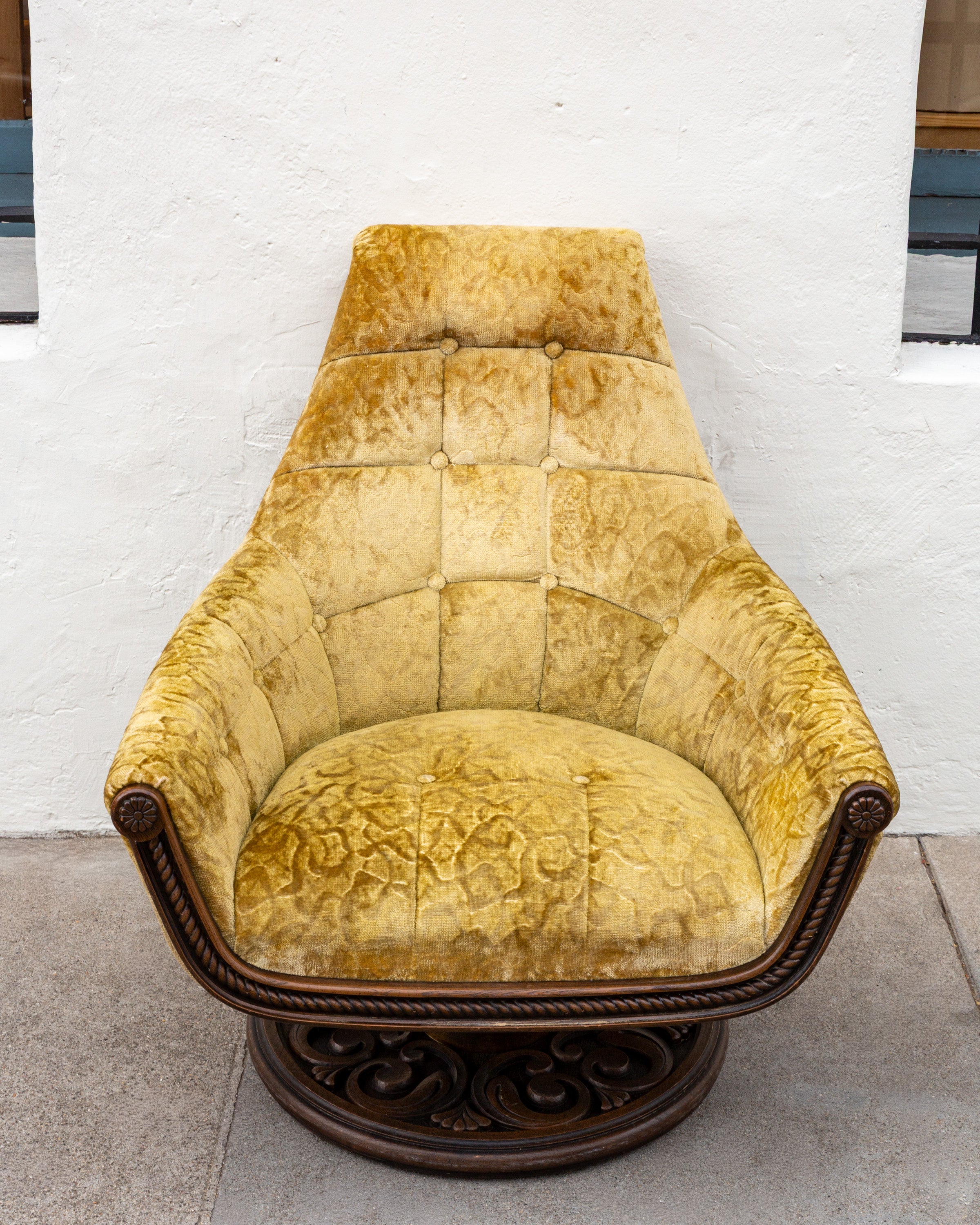 Straight-on front view of the gold velvet swivel chair showing the tapered button-tufted back, rounded seat and round carved base
