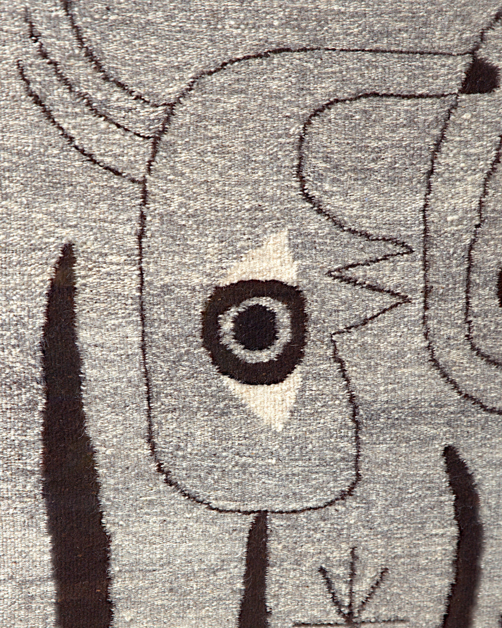 Close detail of the ringed eye on a cream diamond and the thin dark brown outlines in the gray wool weave.