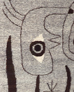 Close detail of the ringed eye on a cream diamond and the thin dark brown outlines in the gray wool weave.