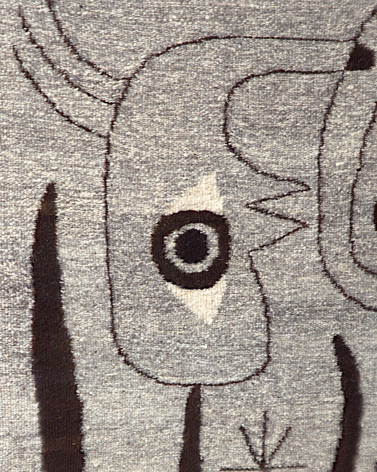 Close detail of the ringed eye on a cream diamond and the thin dark brown outlines in the gray wool weave.