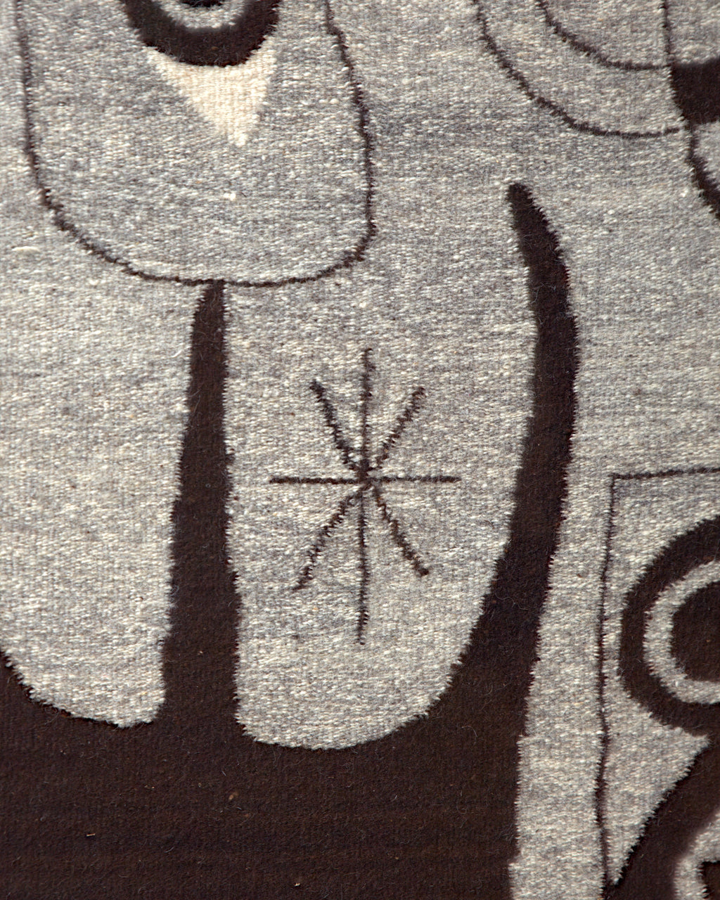 Close detail of the small star motif between dark brown shapes on the gray wool tapestry.