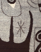 Close detail of the small star motif between dark brown shapes on the gray wool tapestry.