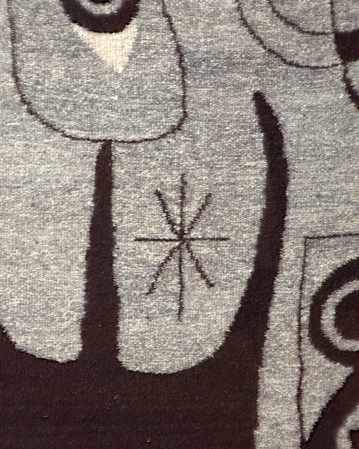 Close detail of the small star motif between dark brown shapes on the gray wool tapestry.
