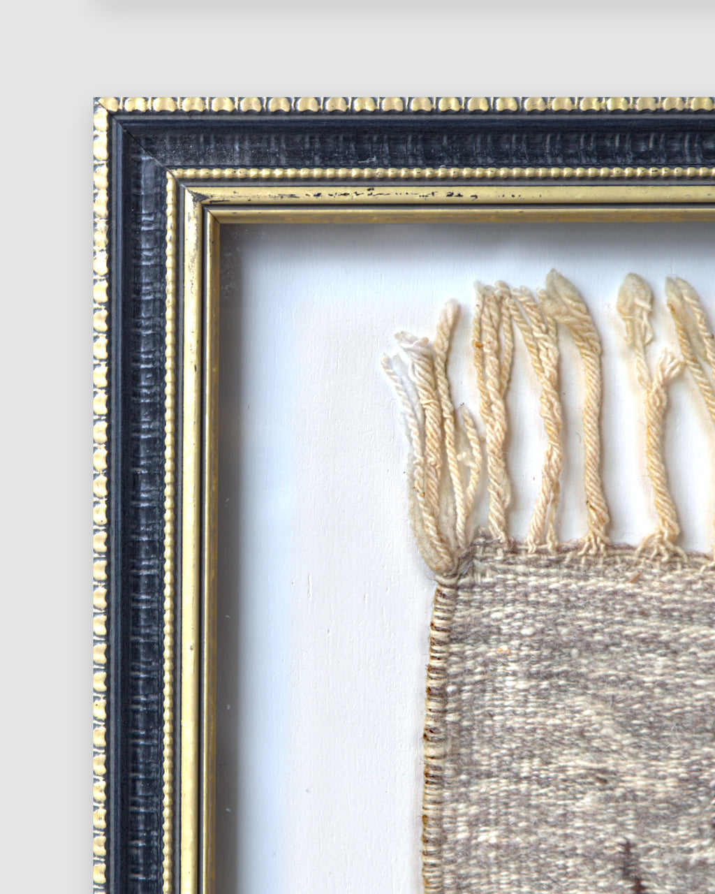 Close view of the upper left frame corner, black with gold beaded edges, on a light gray background.