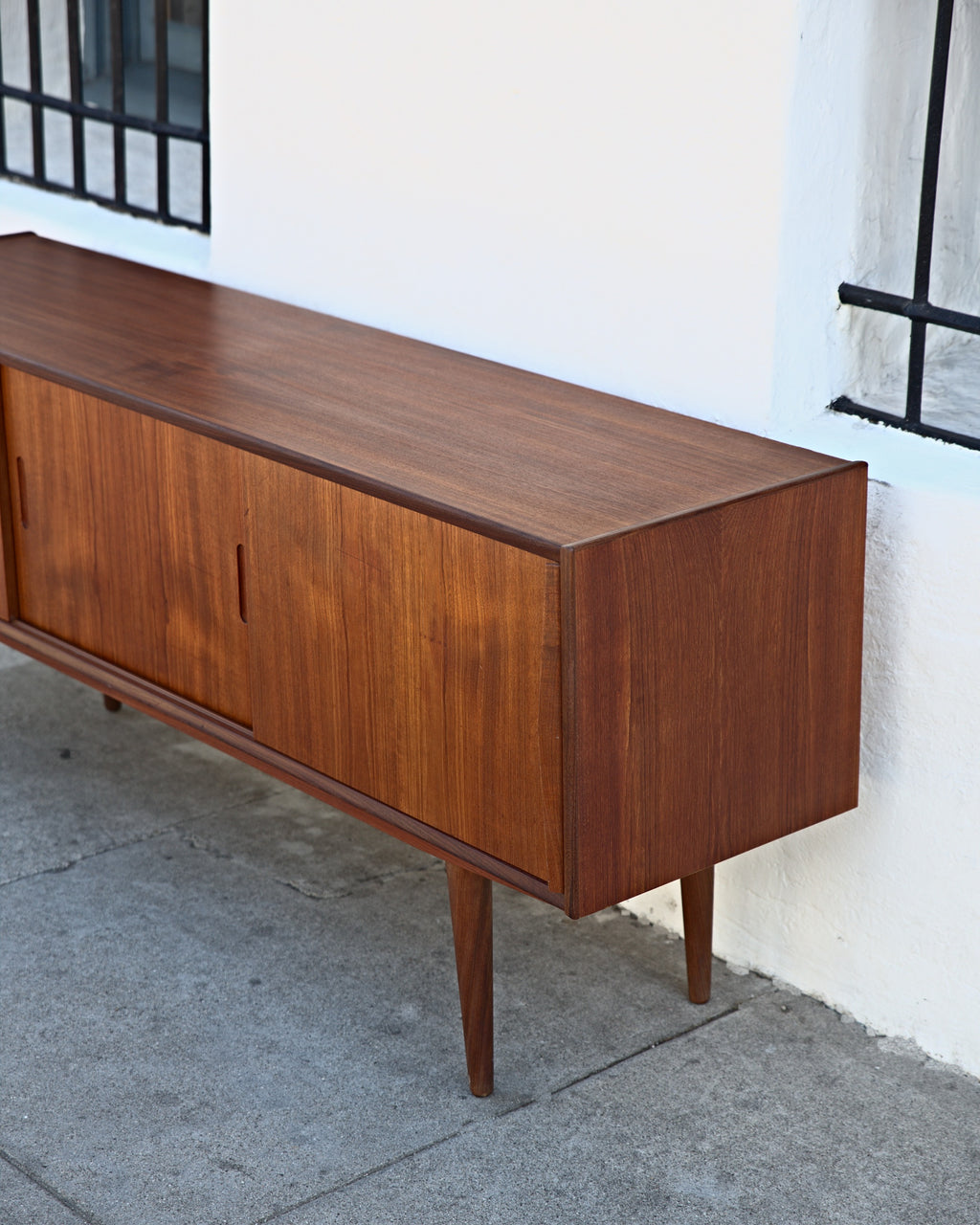 Three-quarter view from the other end of a teak credenza showing the case end and sliding doors