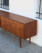 Three-quarter view from the other end of a teak credenza showing the case end and sliding doors