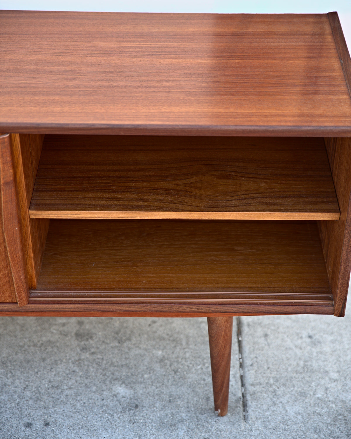 Teak credenza with a door slid open to show an adjustable shelf inside