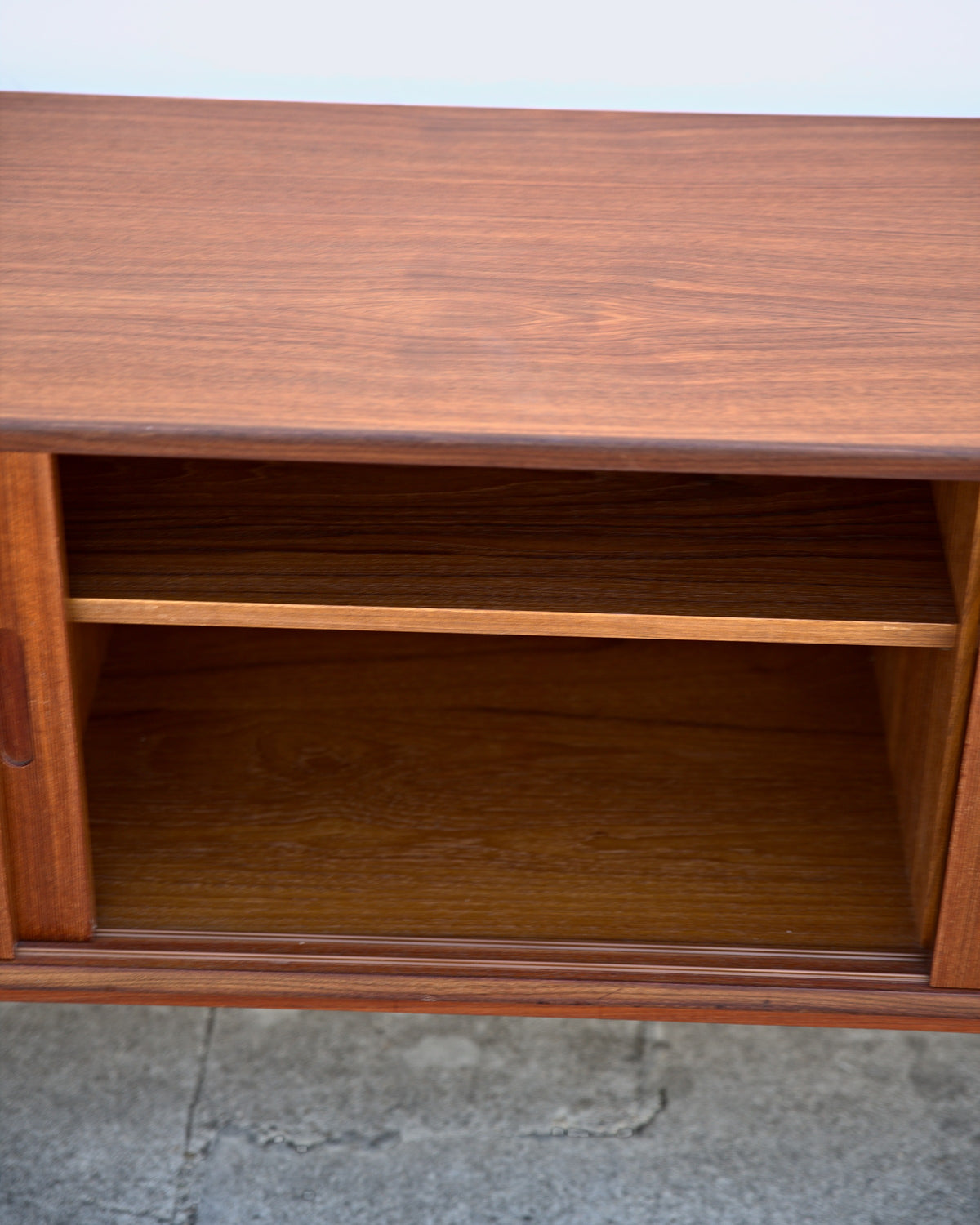 Front view into an open section of a teak credenza with a shelf above a cabinet space