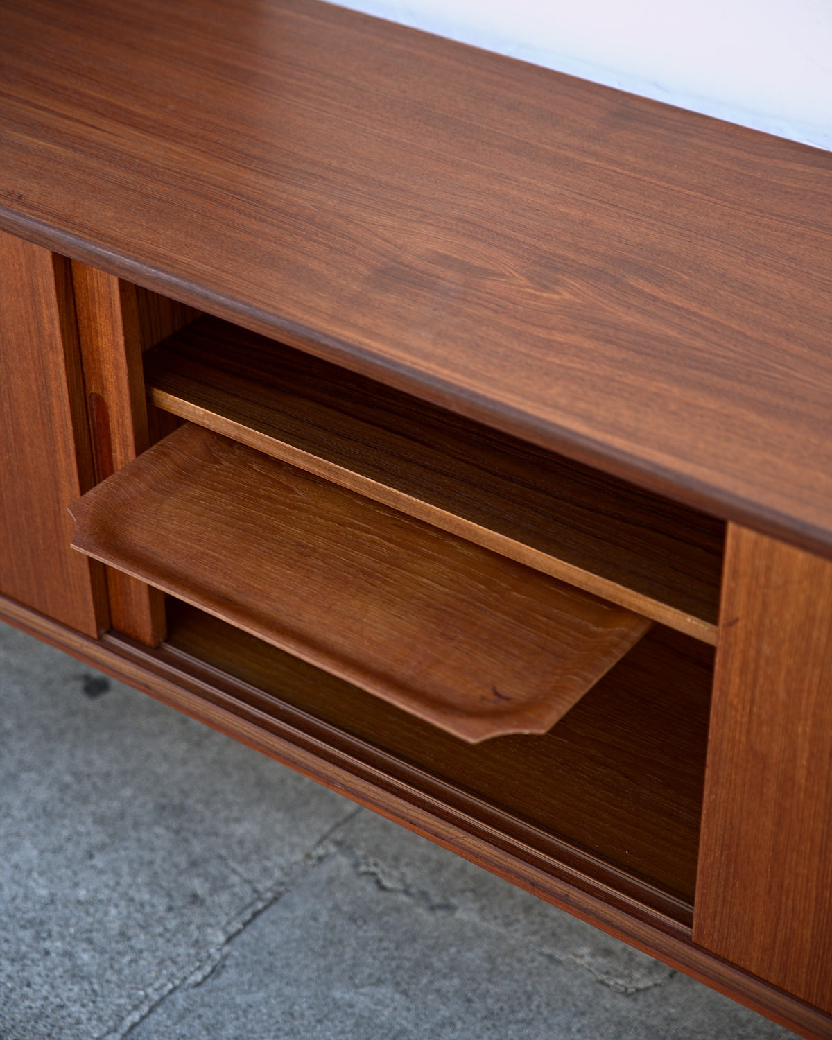 Middle section of a teak credenza with its shelf slid forward and tipped down