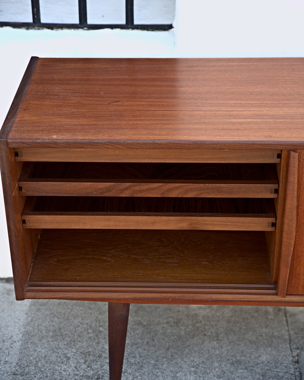 End section of a teak credenza with three stacked pull-out trays over a lower compartment
