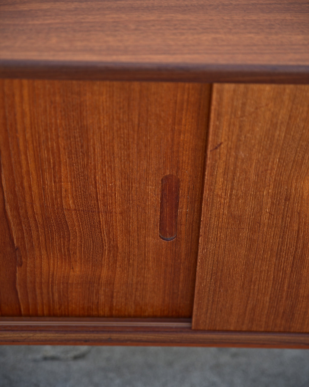 Close-up of a rounded solid teak pull on a sliding credenza door