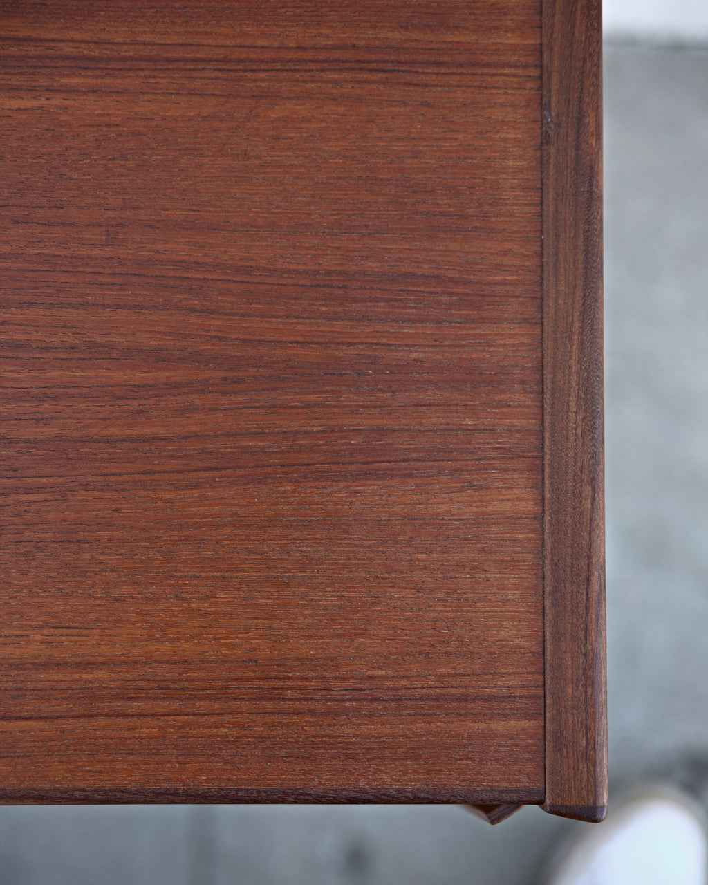 Tight view of the teak top meeting the darker edge band at the end of a credenza