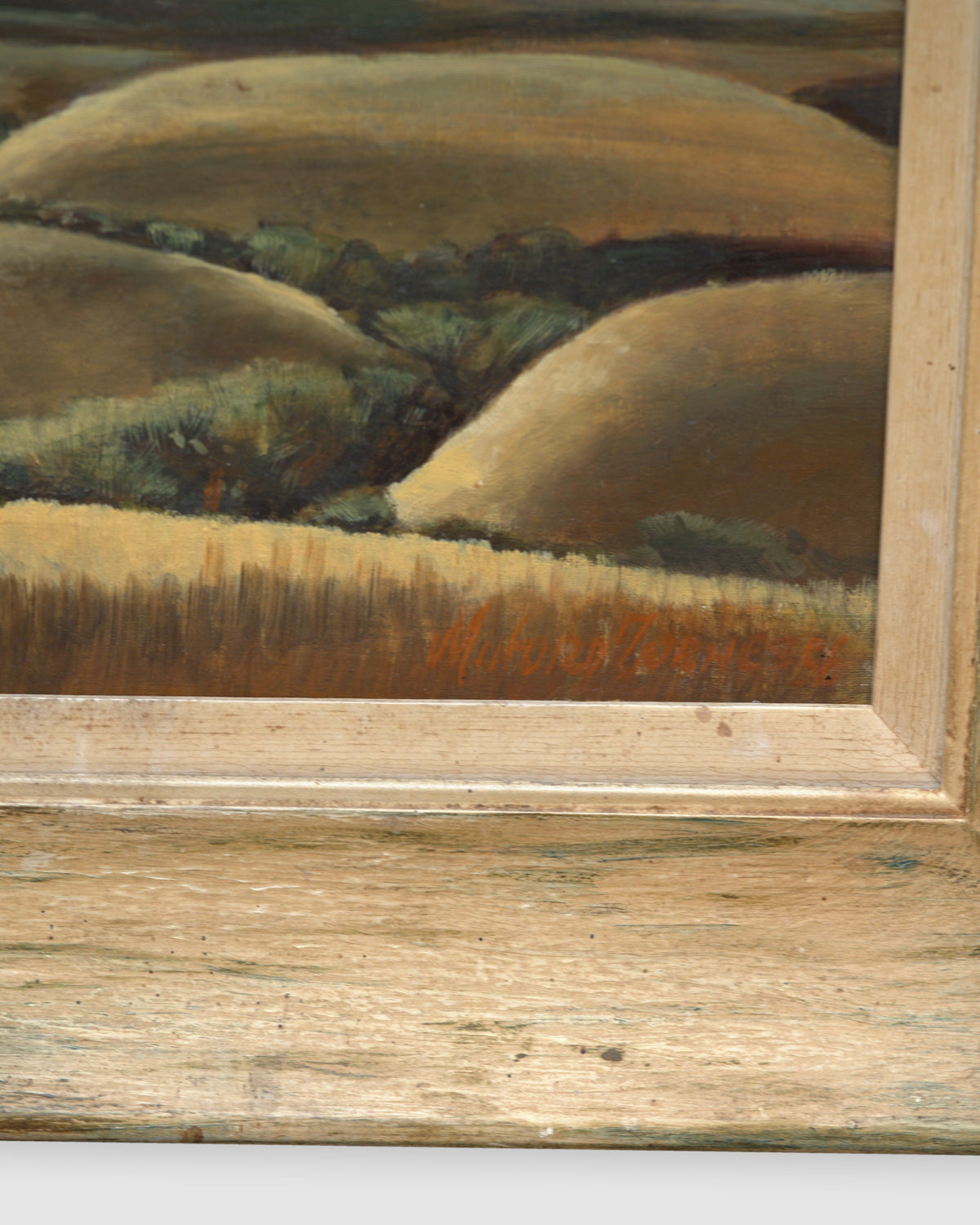 Corner of the frame on the Milford Zornes painting Hills of Nipomo, golden rolling hills under gray clouds, in a wide limed wood frame.